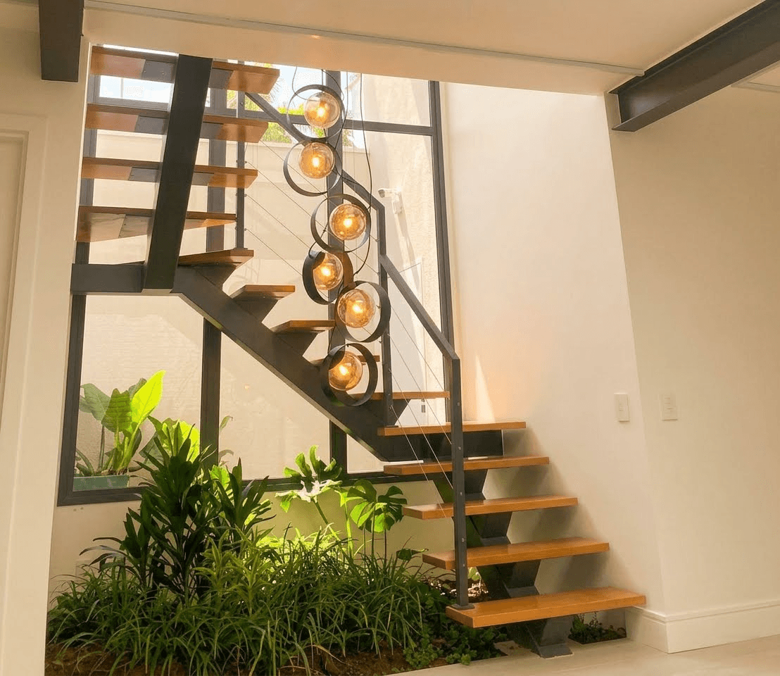 Escada em U com viga central preta, degraus de madeira e guarda-corpo de cabos de aço sobre jardim interno