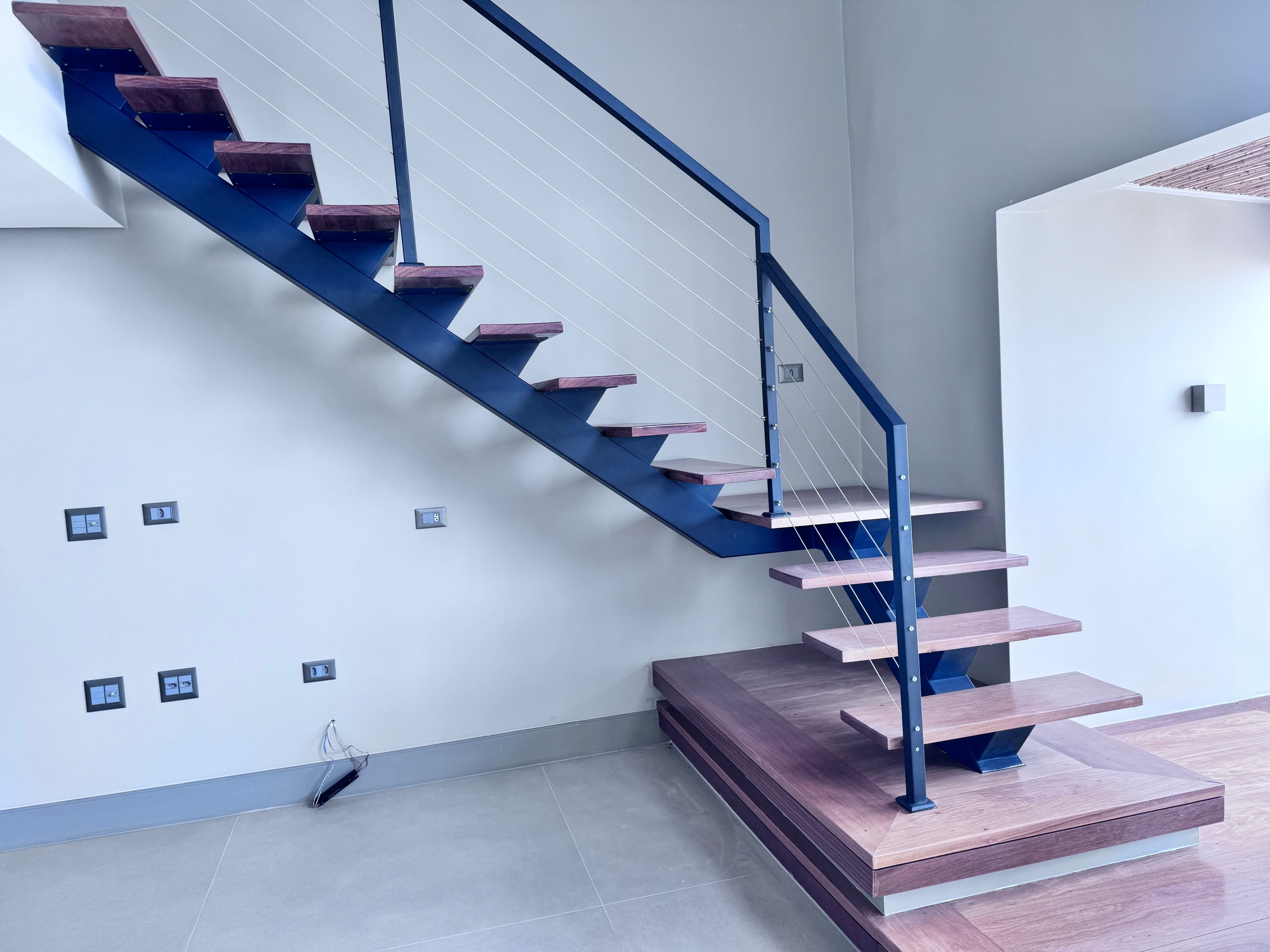 Escada residencial de viga central em L, com degraus em madeira cumaru e guarda-corpo em cabos de aço, projeto da Escadas MV na Vila da Saúde-SP.