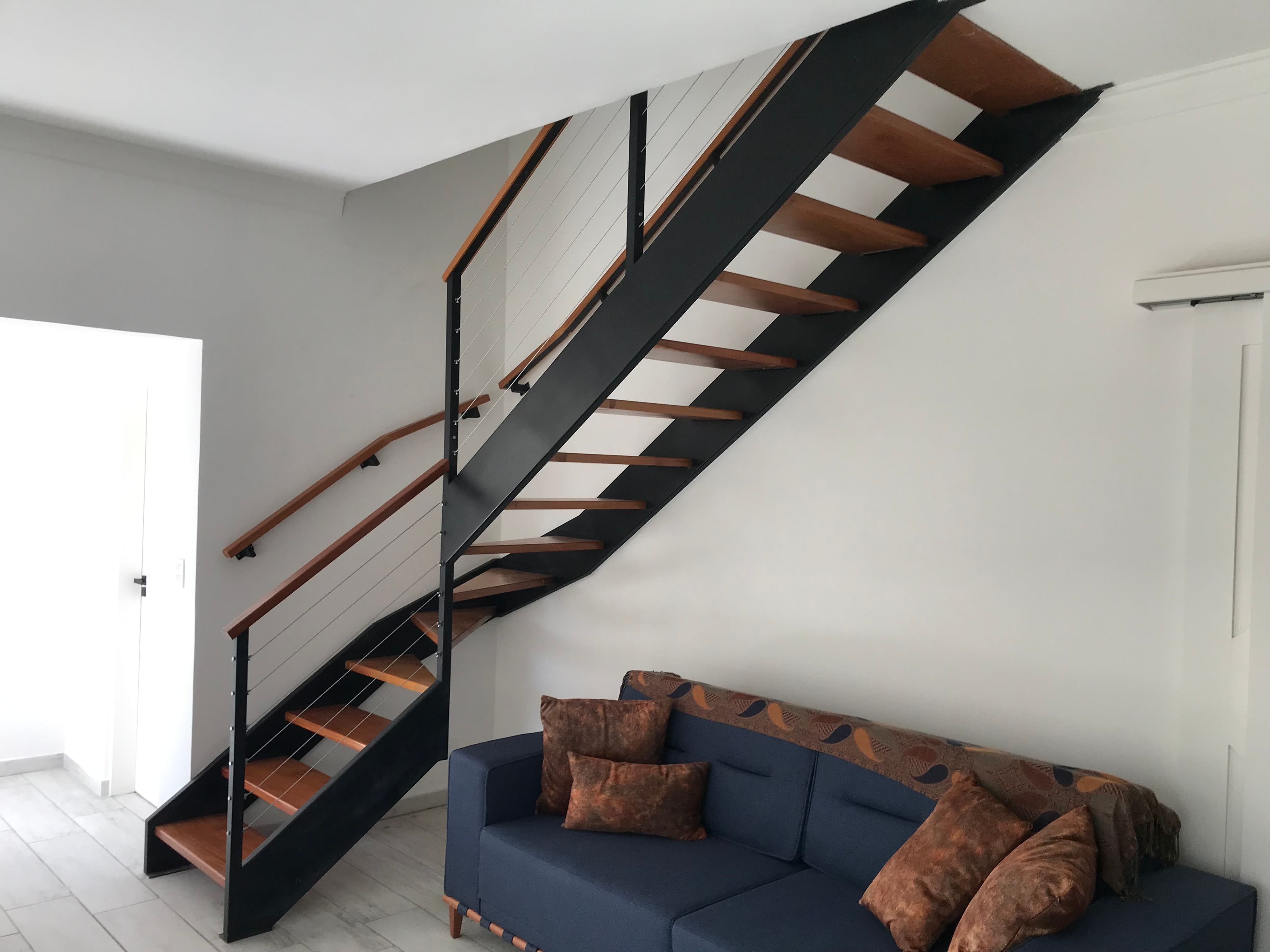 Escada residencial entre vigas em L, com guarda-corpo em cabos de aço e corrimão em madeira, projeto da Escadas MV no Bosque da Saúde, São Paulo-SP.
